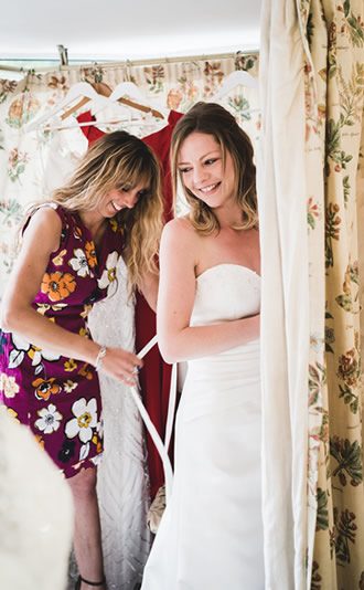Bride Trying Dress On With Assistant